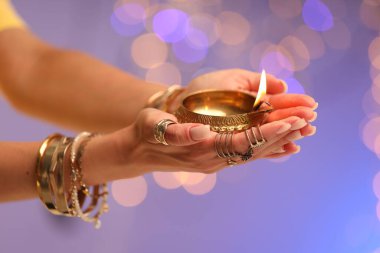 Diwali kutlaması. Renkli arka planda yanan diya lambasını tutan bulanık ışıklı kadın, yakın plan