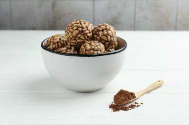 Lezzetli çikolatalı pirinç topları kasede ve kakao tozu beyaz ahşap masada.