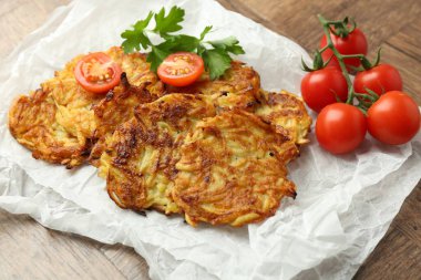 Lezzetli patates krepleri, domatesler ve maydanozlar ahşap masada, yakın plan.