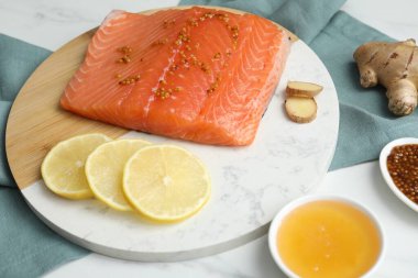 Hardallı somon filetosu, limon dilimleri, beyaz masada bal ve zencefil, yakın plan.