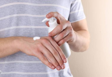 Adam bej arka planda pompa şişesinden el kremi sürüyor, yakın plan.