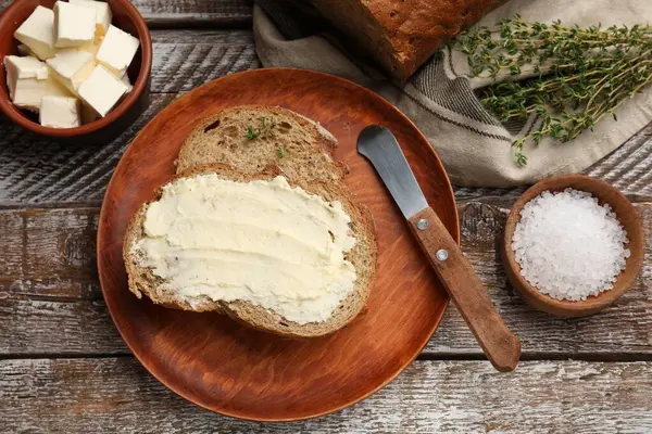 Tereyağlı taze ekmek, kekik, ahşap masada tuz ve bıçak.