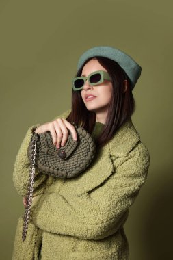 Zeytin arka planında şık aksesuarları olan genç bir kadın.