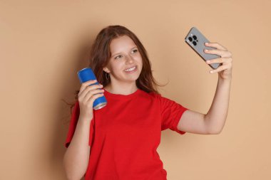 Gülümseyen genç kız bej arka planda selfie çekiyor.