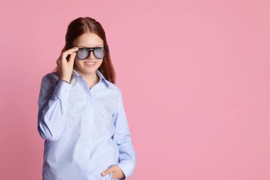 Güneş gözlüklü mutlu genç kız pembe arka planda poz veriyor. Metin için boşluk