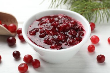 Lezzetli kızılcık sosu kasede, böğürtlen ve köknar dalları beyaz ahşap masada, yakın plan.