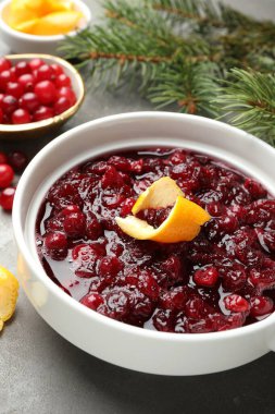 Lezzetli kızılcık sosu kasede, portakal kabuğu, böğürtlen ve köknar dalları gri masada, yakın plan.