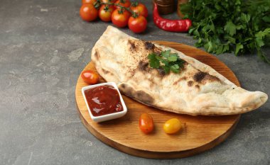 Lezzetli calzone, domates, sos ve maydanozlu masa, yakın plan.