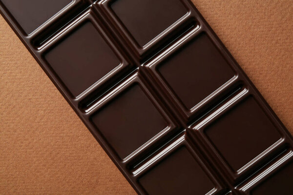 Tasty chocolate bar on brown background, top view