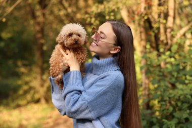 Sonbahar parkında sevimli köpeğiyle gülümseyen kadın.