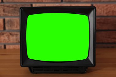 Tuğla duvarın yanındaki ahşap masada yeşil ekranlı Retro TV seti. Krom anahtar
