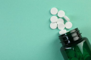 Turkuaz arka planda antibiyotik hapları olan bir ilaç şişesi. Metin için boşluk