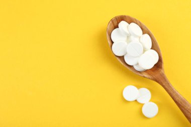 Sarı arka planda kaşıkta antibiyotik haplar, üst manzara. Metin için boşluk