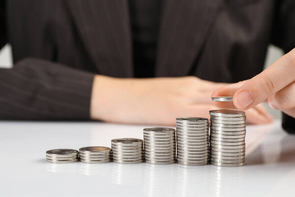 Salary concept. Woman putting coin on stack at white table, closeup