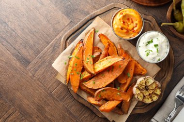 Ahşap masada sosla servis edilen lezzetli pişmiş tatlı patatesler. Metin için boşluk