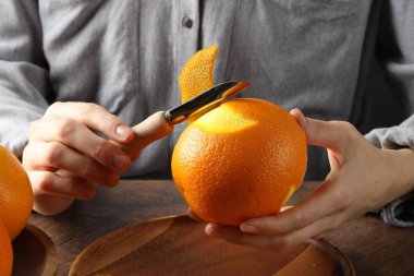 Woman zesting orange at wooden table, closeup clipart