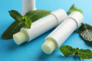 Açık mavi arka planda doğal dudak kremleri ve nane yaprakları, yakın plan.