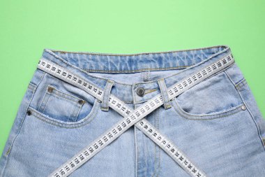 Yeşil arka planda kot pantolon ve mezura, üst görünüm