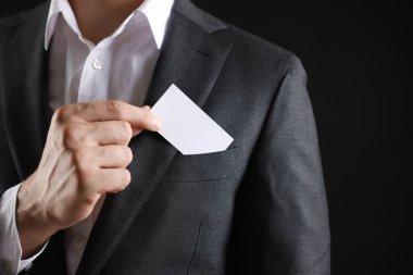Siyah arka planda ceketinin cebinden boş kartvizit alan adam, yakın plan. Tasarım için model