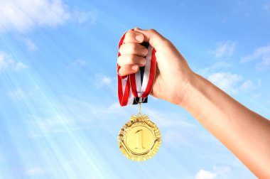 Altın madalyayı elinde tutan kadın gökyüzüne karşı, yakın plan