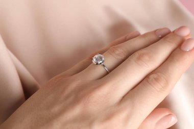 Bej kumaşa karşı değerli taşlı güzel bir yüzük takan kadın, yakın plan.