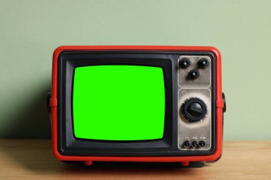 Soluk renkli duvarın yanındaki ahşap masada yeşil ekranlı Retro TV seti. Krom anahtar