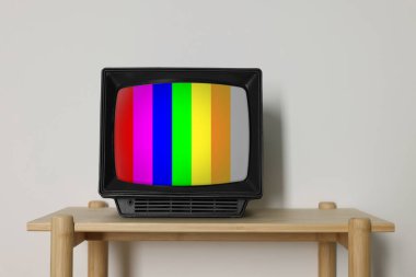 Beyaz duvarın yanındaki ahşap masada test kalıplı Retro TV seti. Ekrandaki renk çubukları. Sinyal yok.
