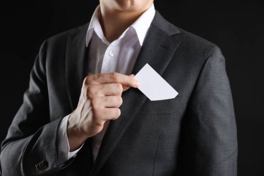 Siyah arka planda ceketinin cebinden boş kartvizit alan adam, yakın plan. Tasarım için model