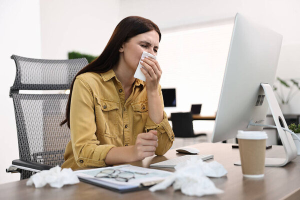 Sick woman with runny nose at table in office