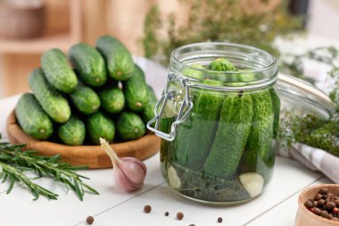 Kavanozda salatalık turşusu, beyaz ahşap masada sarımsak ve biber, yakın plan.