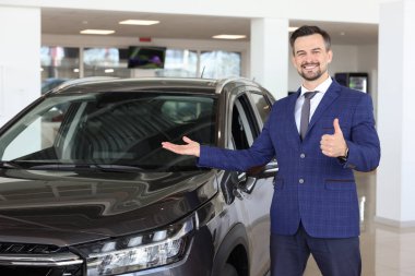 Kuaförde yeni siyah arabanın yanında baş parmak gösteren mutlu bir satıcı.