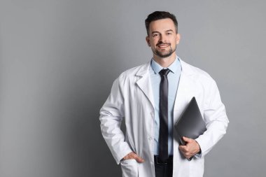 Gri arka planda dizüstü bilgisayarı olan gülümseyen doktor.