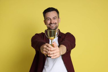 Sarı arka planda altın kupa ile mutlu kazanan.