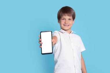 Açık mavi arka planda akıllı telefonu olan şirin bir çocuk.