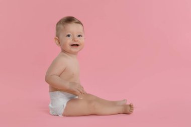 Pembe arka planda oturan, bebek bezi takmış şirin bir bebek.