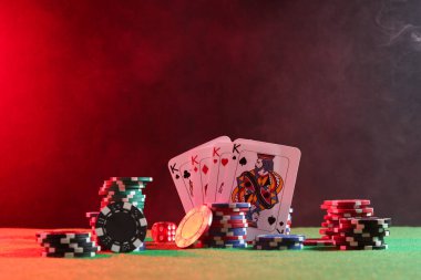Neon ışıklarıyla yeşil masada poker fişleri, zarlar ve iskambil kartları