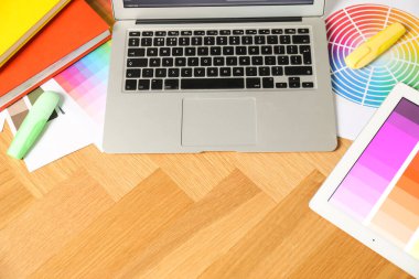 Dizüstü bilgisayarı, tableti, paletleri ve ahşap masadaki kırtasiyesi olan tasarımcının çalışma yeri