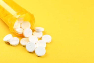 Sarı arka planda antibiyotik hapları olan bir ilaç şişesi, yakın plan. Metin için boşluk
