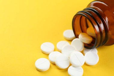 Sarı arka planda antibiyotik hapları olan bir ilaç şişesi, yakın plan. Metin için boşluk