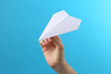 Açık mavi arka planda beyaz kağıt uçaklı kadın, yakın plan.