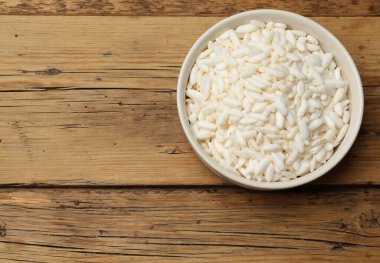 Puffed rice in bowl on wooden table, top view. Space for text clipart