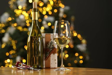 Şarap cam, şişe, kanat tirbuşonu ve Noel hediyesi ahşap masada bulanık ışıklara karşı.