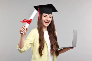 Mezuniyetten sonra bilgisayarı ve diploması olan mutlu bir öğrenci.