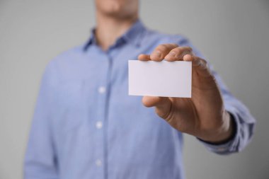 Gri arka planda boş bir kartvizit tutan adam, yakın plan. Tasarım için model