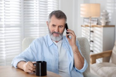 Elinde bir bardak içki olan son sınıf öğrencisi kapalı bir masada akıllı telefondan konuşuyor.