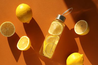 Limonlu su şişede, meyveler kahverengi arka planda, düz yerde.