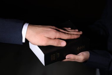 Man taking oath with his hand on Bible against black background, closeup clipart