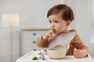 Evdeki yüksek sandalyede sağlıklı yiyecekler yiyen şirin bir bebek.