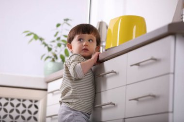 Küçük çocuk mutfakta tost makinesiyle oynuyor, düşük açılı. Tehlikeli bir durum.