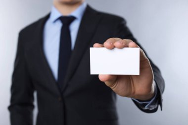 Gri arka planda boş bir kartvizit tutan adam, yakın plan. Tasarım için model
